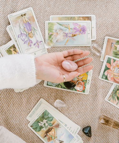 A womans hand holding a stone above a spread of tarot cards on the contact page for Long Beach Tarot Reading Service Wise Path Tarot